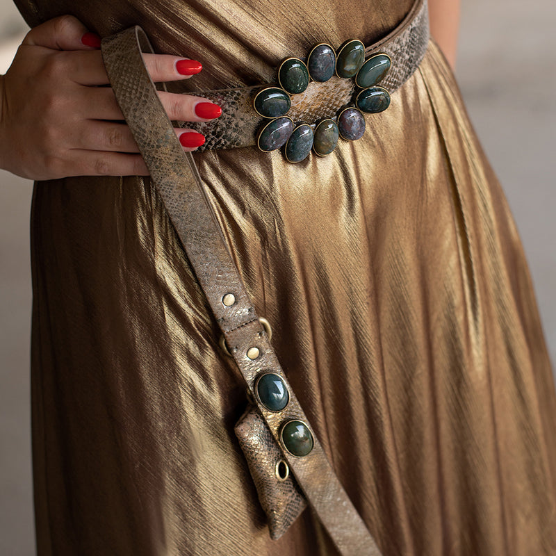 Une femme chic porte à la taille une ceinture assortie à la laisse de son chien en cuir de buffle et décorée de pierres vertueuses